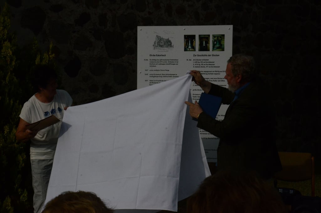 Wilma Schulz, Vorsitzende des Heimat- und Kulturfördervereins Kakerbeck, und Pfarrer Dieter Borchert enthüllen die neue Tafel neben der Kirche.