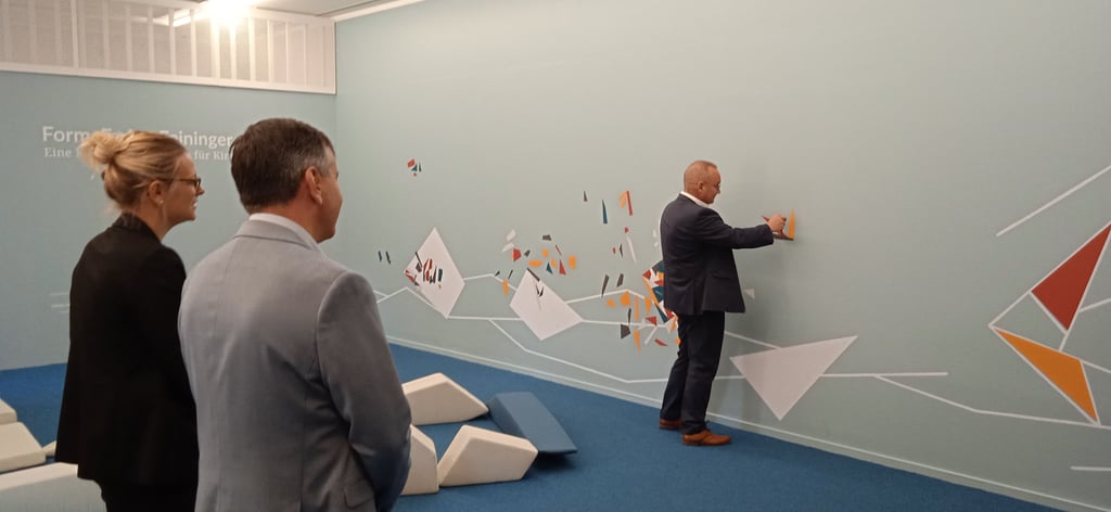 Galeriedirektorin Gloria Köpnick und Landrat Thomas Balcerowski sehen Oberbürgermeister Frank Ruch beim Bilderlegen zu.