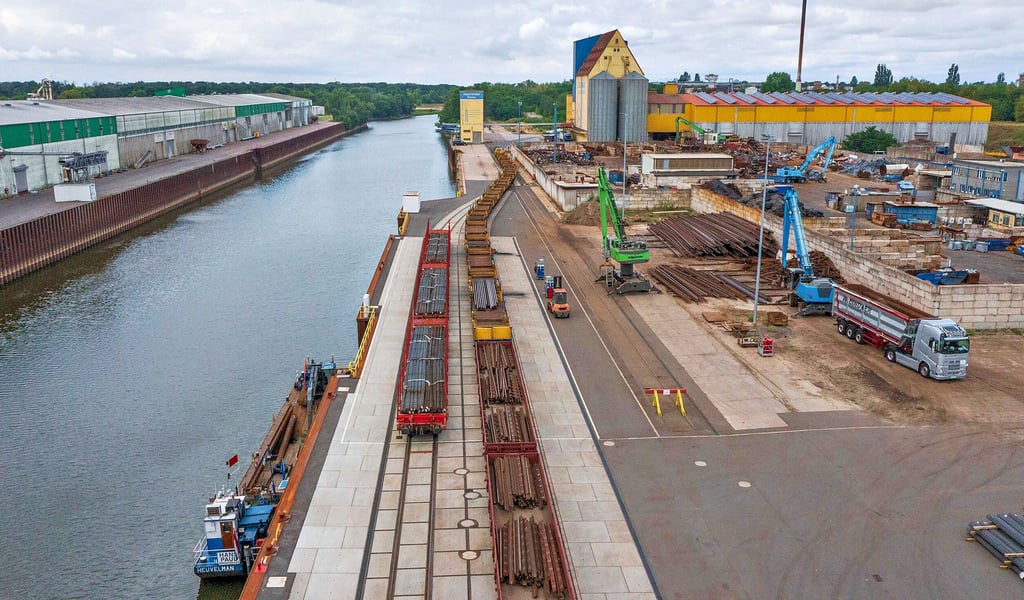 Auf dem Kai reihen sich die zu entladenen Waggons, im Wasser wartet ein einzelnes Arbeitsschiff auf einen Einsatz.