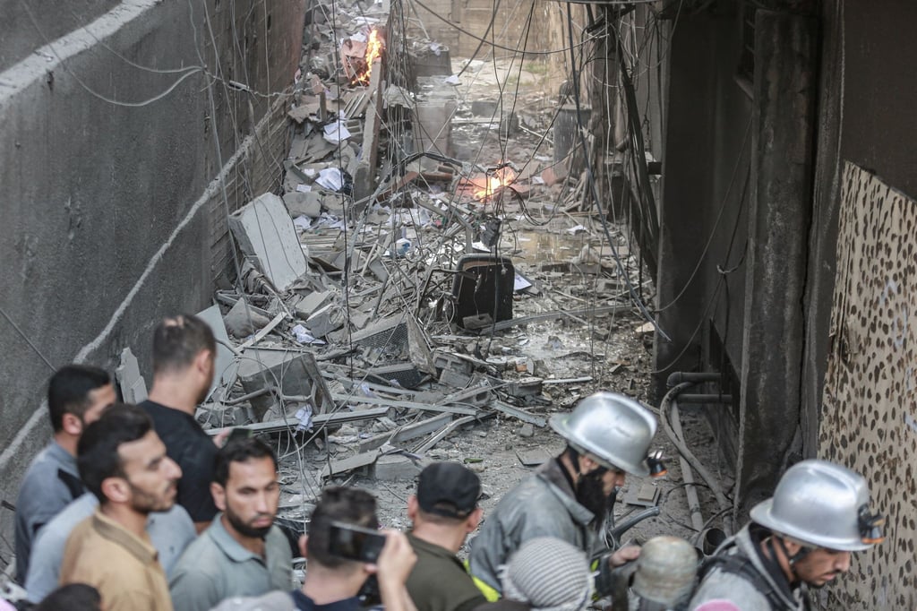 Männer und zwei Feuerwehrleute stehen nach einem israelischen Luftangriff vor Trümmern. Bei Angriffen des israelischen Militärs auf den Gazastreifen sind palästinensischen Angaben zufolge mehrere Menschen getötet worden.
