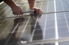 Ein Arbeiter montiert Photovoltaikmodule auf dem Dach eines Wohnhauses.