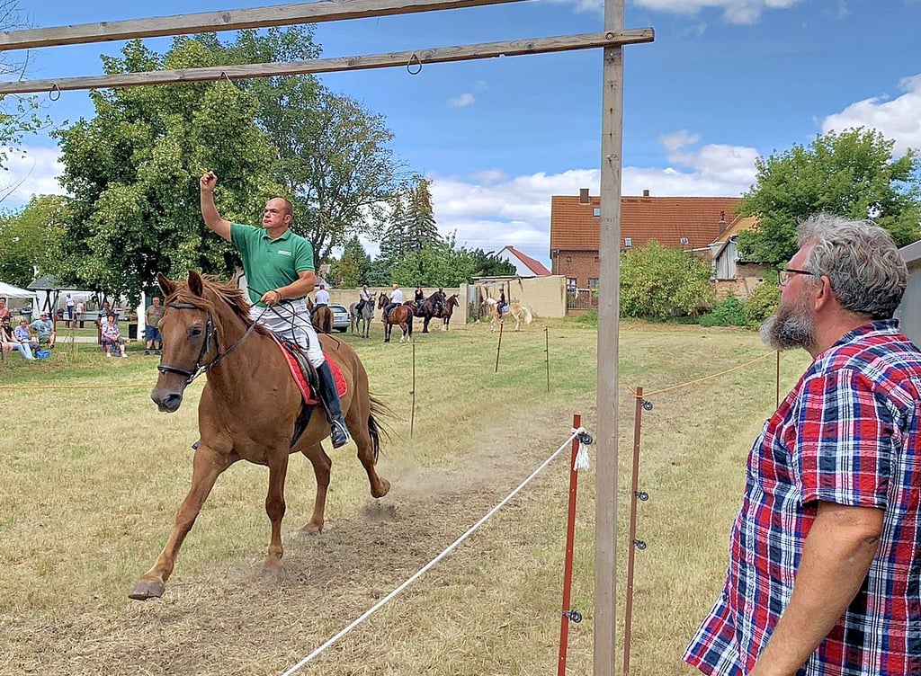 Frank Wischnewski (r.) vom Heimatverein beobachtet beim Sommerfest in Trebbichau an der Fuhne einen Teilnehmer des Ringreitens.