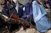 Ein Taliban-Kämpfer hält sein Gewehr in der Hand, während Menschen in Kabul auf die Verteilung von Lebensmittelrationen durch eine Hilfsorganisation warten.