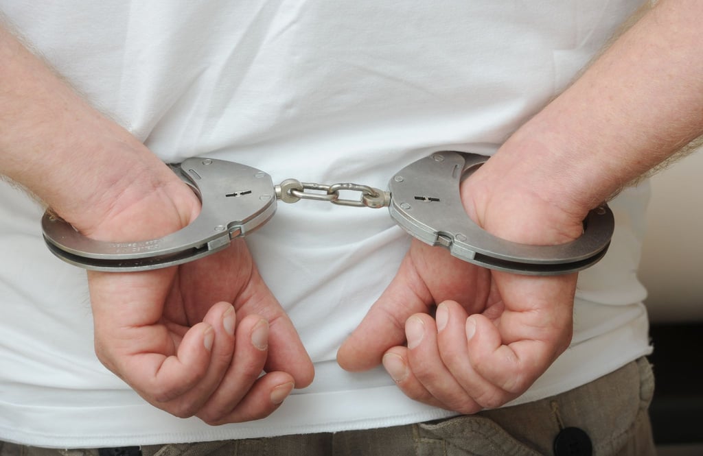 Zwei männliche Hände sind in Polizeihandschellen gefesselt.