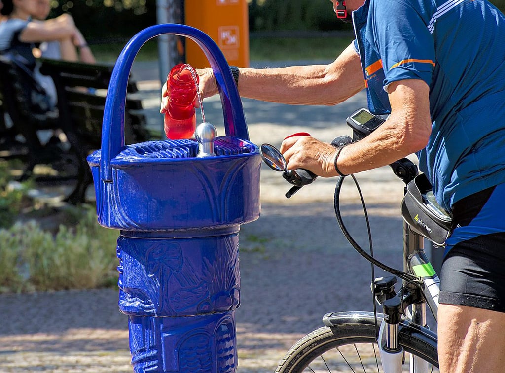 Ein Radfahrer füllt an einem Trinkbrunnen seine Wasserflasche auf.