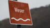 Ein Verkehrsschild „Weser“ ist an einer Brücke über dem Fluss befestigt.