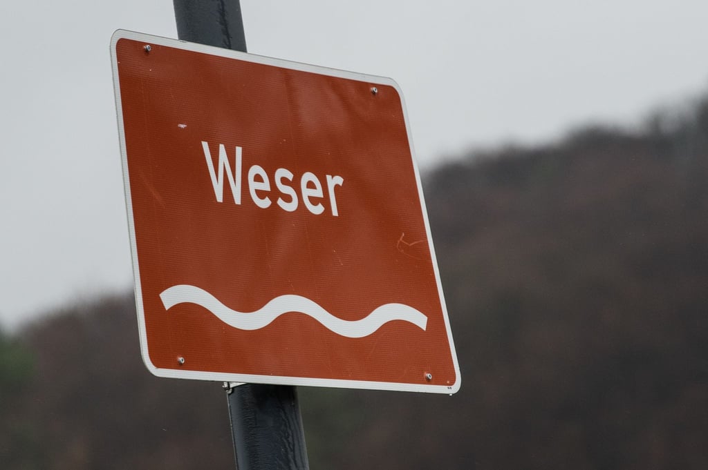 Ein Verkehrsschild „Weser“ ist an einer Brücke über dem Fluss befestigt.