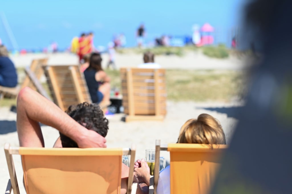 Zwei Gäste der Beachbar am Naturstrandt genießen den Blick auf die Nordsee bei einem Kaltgetränk.