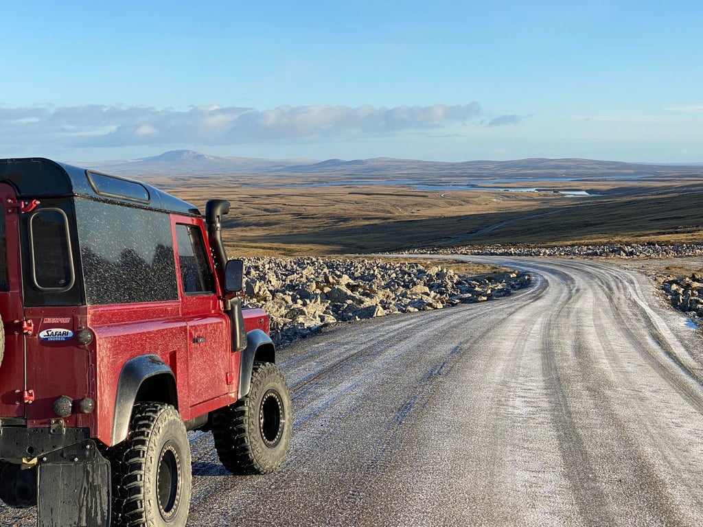 Ein roter Rover, ein Defender 90, steht auf einer Landstraße.