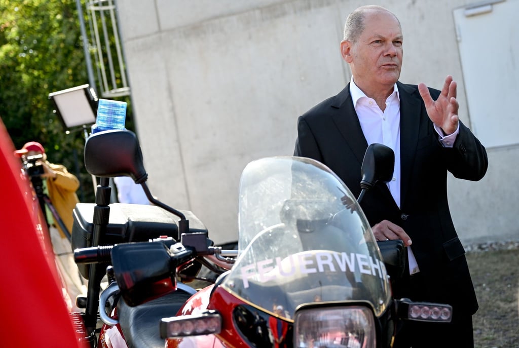 Bundeskanzler Olaf Scholz steht neben einem Motorrad der freiwilligen Feuerwehr Beelitz.