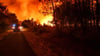Ein Feuerwehrfahrzeug fährt auf einer Straße an den Flammen eines Waldbrandes in der Nähe von Belin-Beliet vorbei.