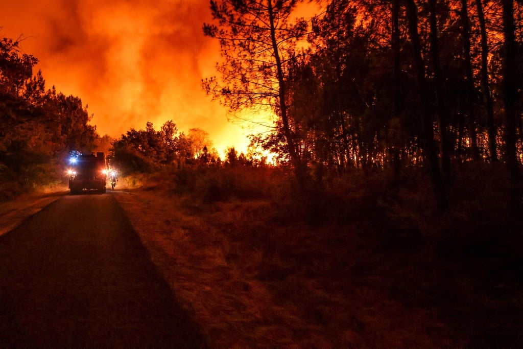 Ein Feuerwehrfahrzeug fährt auf einer Straße an den Flammen eines Waldbrandes in der Nähe von Belin-Beliet vorbei.