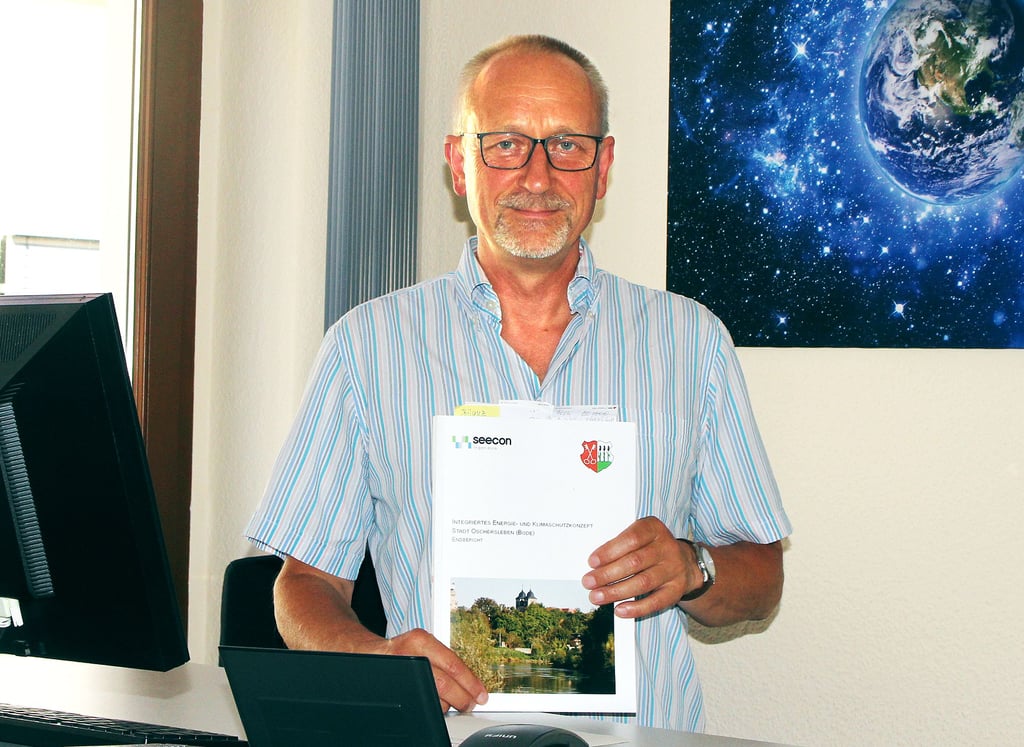 Passend zum neuen Aufgabenbereich hat Thomas Neumann auch sein Büro im Oschersleber Rathaus mit einem eindrucksvollen Bild von der Erde ausgestattet. In der Hand hält er das Klimaschutzkonzept der Stadt Oschersleben, eine seiner Arbeitsgrundlagen.