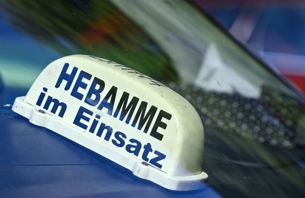 Ein Schild mit der Aufschrift „Hebamme im Einsatz“ liegt in einem Auto.