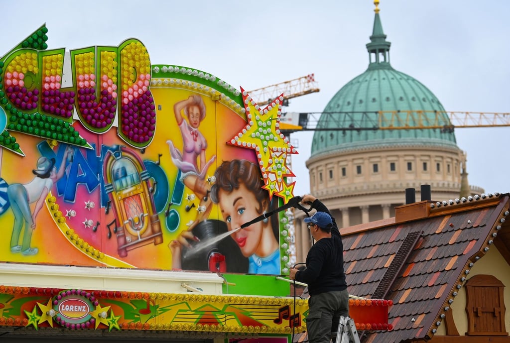 Ein Schausteller reinigt die bunt bemalte Fassade an seinem Stand.