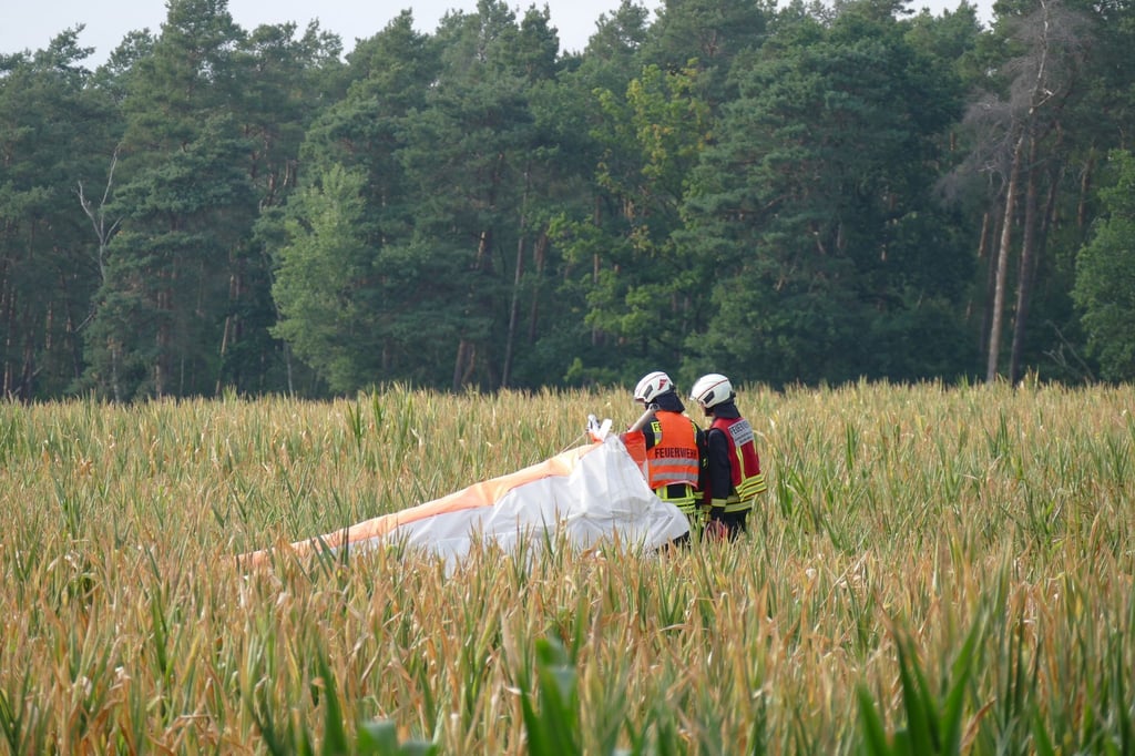 Einsatzkräfte der Feuerwehr stehen auf einem Feld am Absturzort von einem Leichtdrachen.