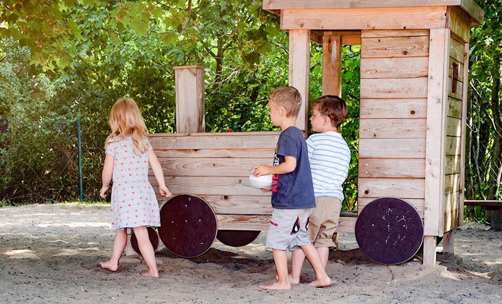 Kinder spielen im Schatten der Bäume. Hier und fast überall auf dem Außengelände ist Sand der Spieluntergrund.