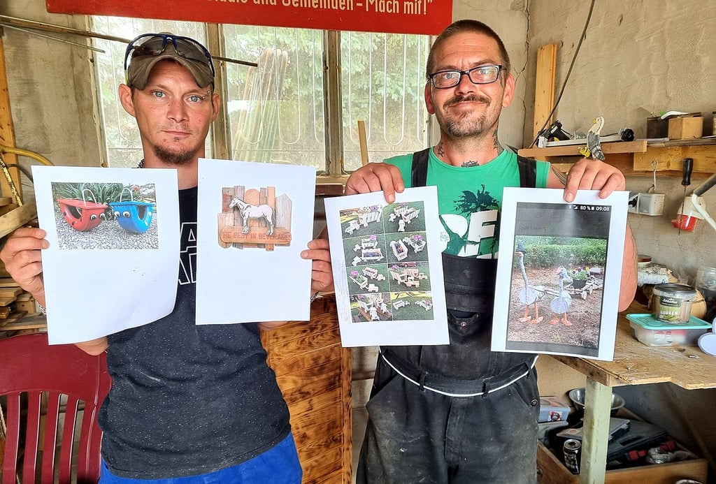 Die beiden Männer in der Holzwerkstatt der Deutschen Angestellten-Akademie in Havelberg zeigen Bilder von weiteren anspruchsvollen Projekten, die sie verwirklichen wollen.