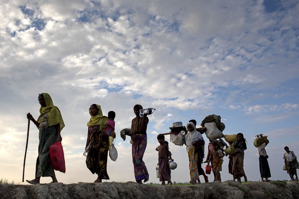 Rohingya-Flüchtlinge gehen mit ihrem Gepäck über ein Reisfeld in Bangladesch.