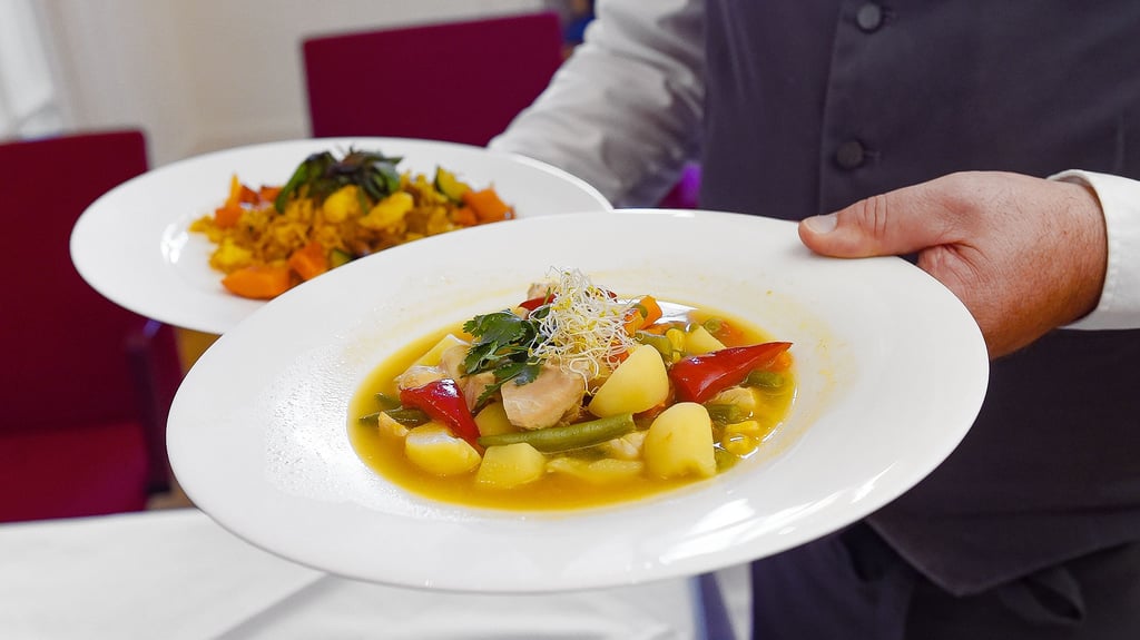 Ein Kellner serviert ein Reisgericht und einen Eintopf. In vielen Restaurants und Hotels fehlt Personal.