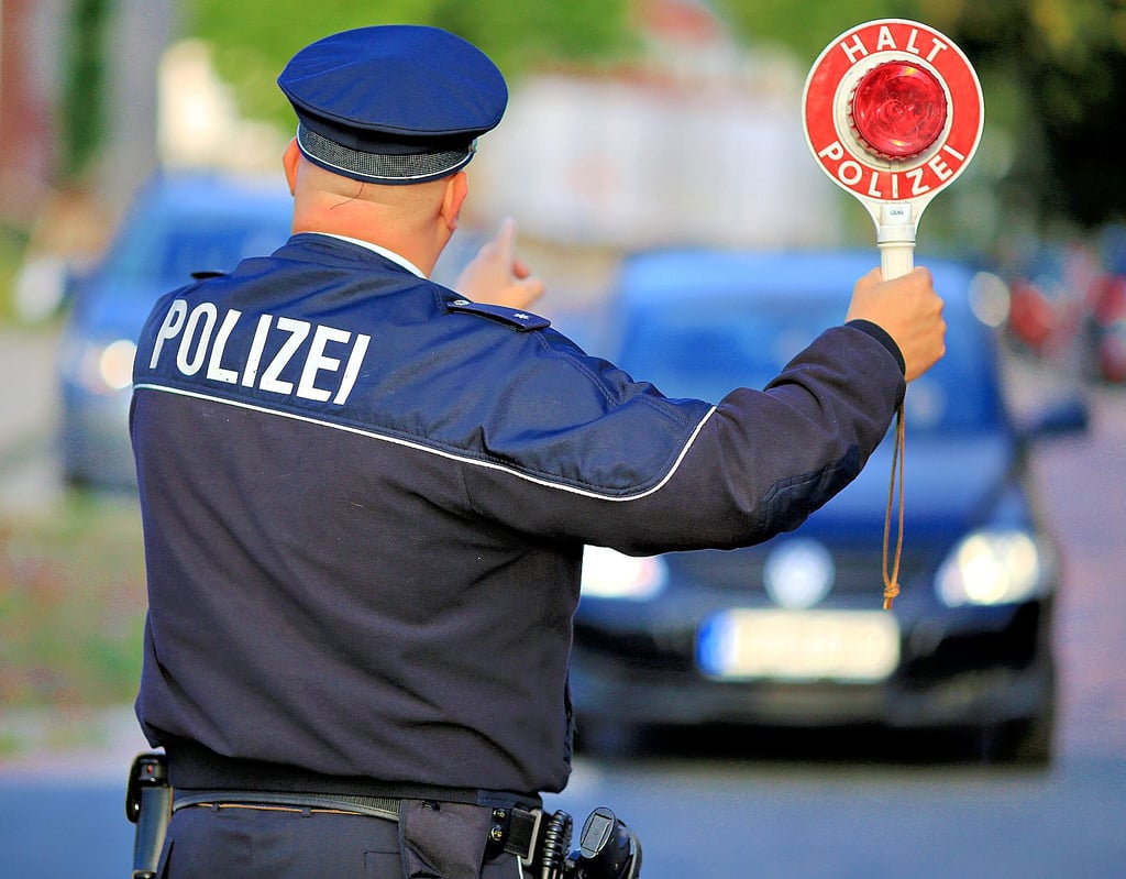 Ein Polizist hält einem Autofahrer eine Kelle „Halt Polizei“ entgegen.