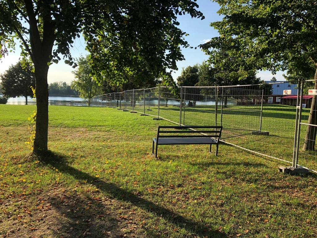 Mitten im Erholungspark teilen Bauzäune das Gelände, die bis zum Wasser verlaufen.