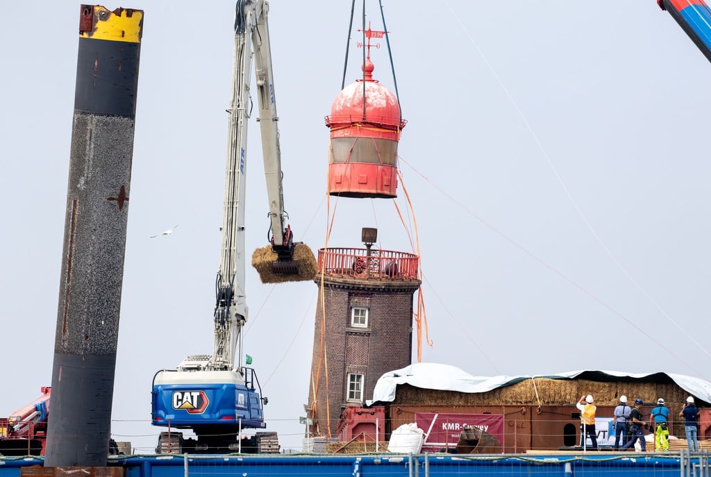 Ein Kran hebt die historische Kuppel von dem schiefen Leuchtturm auf der Mole ab.