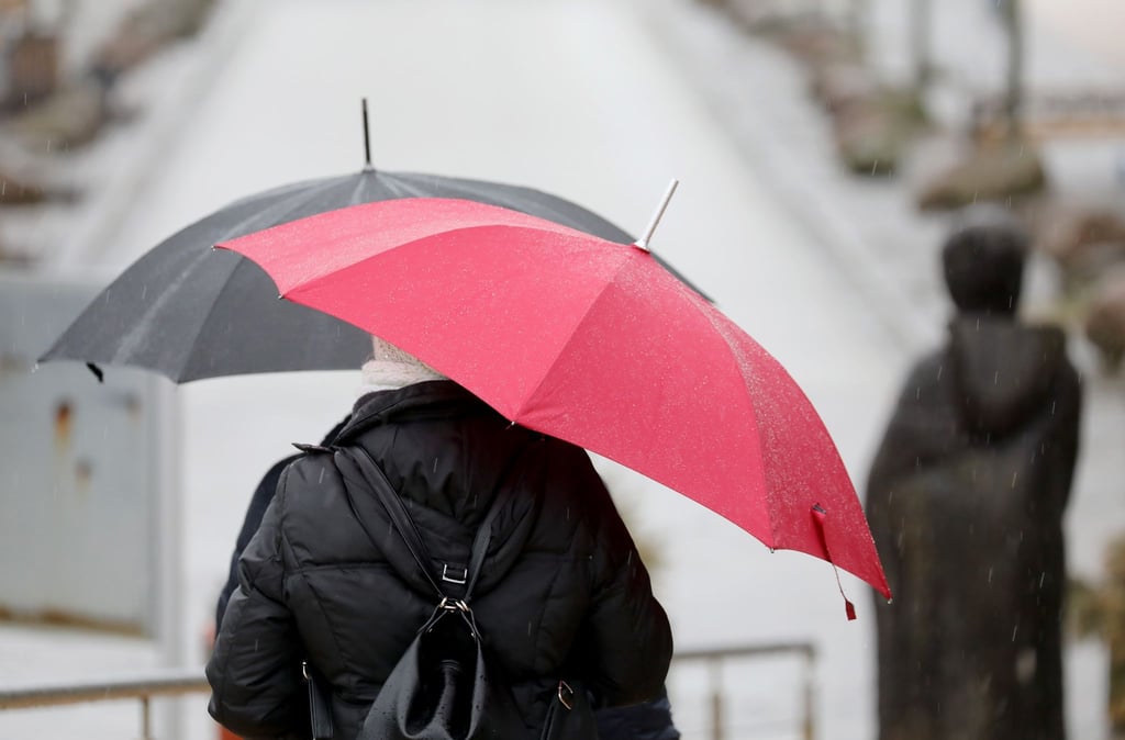 Passanten mit Regenschirmen gehen über eine Promenade.
