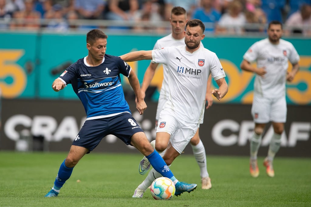 Darmstadts Fabian Schnellhardt (l) schirmt den Ball vor dem heraneilenden Heidenheimer Denis Thomalla ab.