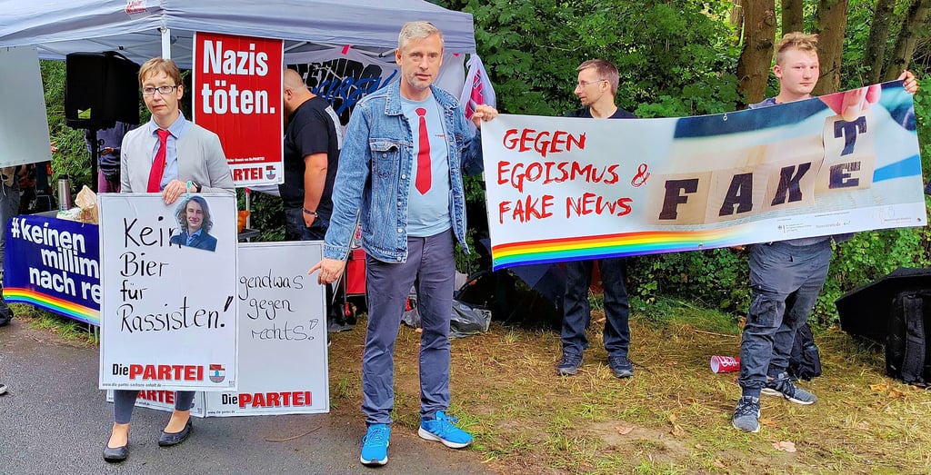 Demonstranten von „Die Partei“ haben sich vor dem Grundstück Poggenburgs in Stößen, auf dem Rechte feiern, mit Protestschildern aufgestellt.