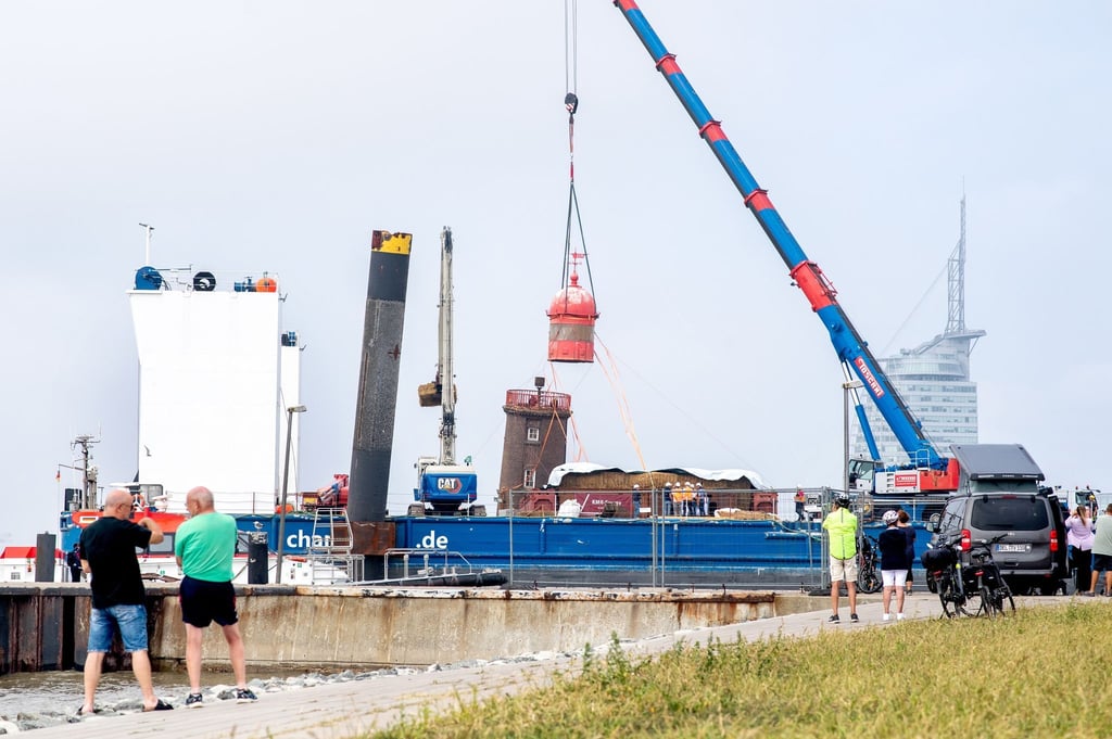 Ein Kran hebt die historische Kuppel von dem schiefen Leuchtturm auf der Mole ab.