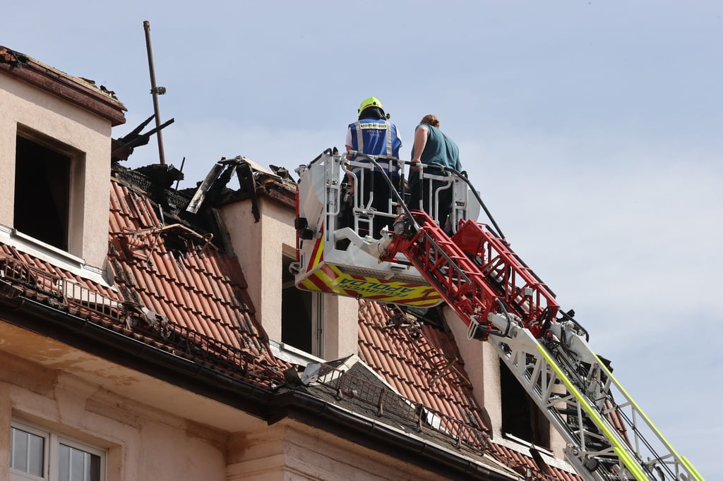 Feuerwehrleute und Statiker untersuchen das Dach eines Mehrfamilienhauses von einer Drehleiter aus. Beim Brand des Mehrfamilienhauses sind am frühen Sonntag mindesten vier Personen getötet und 13 Menschen verletzt worden.
