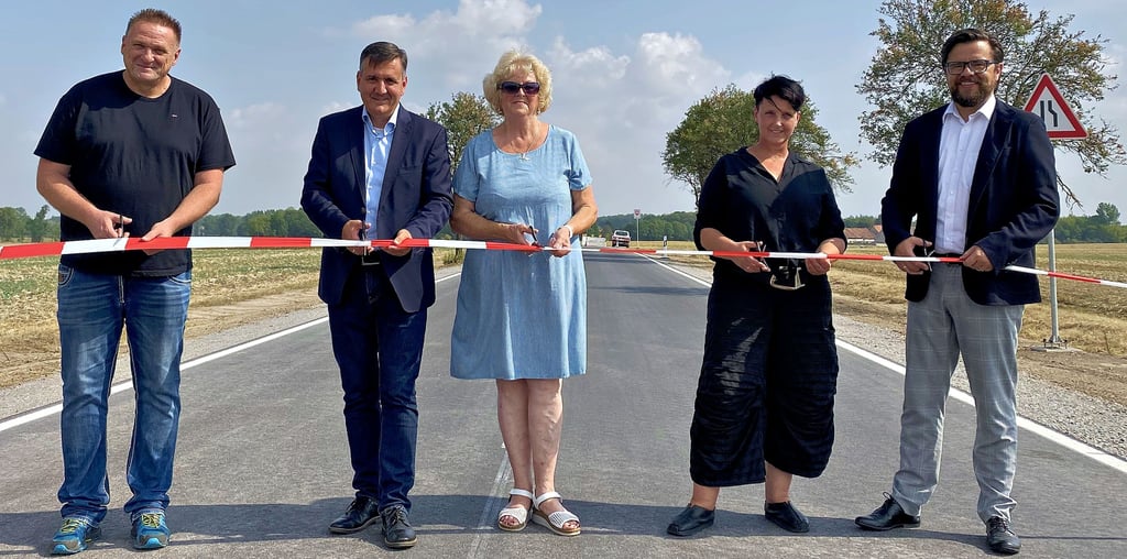 Landrat Thomas Balcerowski (2. v. l), Ortsbürgermeisterin Waltraud Beck (Mitte), Tiefbautechnikerin Karin Bergmann-Schmidt vom Kreisstraßenamt (2. v. r) und Huy-Bürgermeister Maik Berger (rechts) geben im Beisein eines Vertreters der Baufirma (links) mit symbolischem Scherenschnitt die Straße Richtung Neudamm frei.
