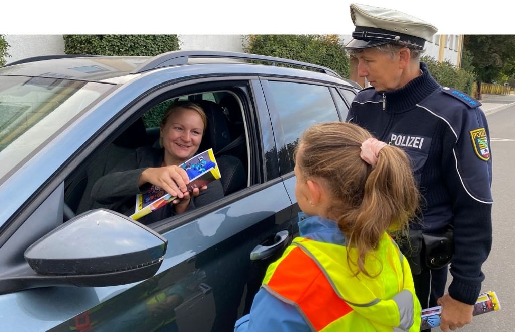 Die Drittklässlerin Annelie übergibt im Beisein von Regionalbereichsbeamtin Ilka Linkohr eine Zuckerüte plus Flyer an Sandra Dannenberg, die extra langsam an der Grundschule vorbeifuhr und auf Schüler und Abc-Schützen achtete.