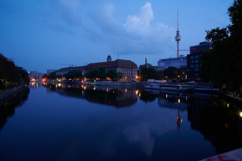Lichter und Gebäude spiegeln sich in der Spree am frühen Morgen.