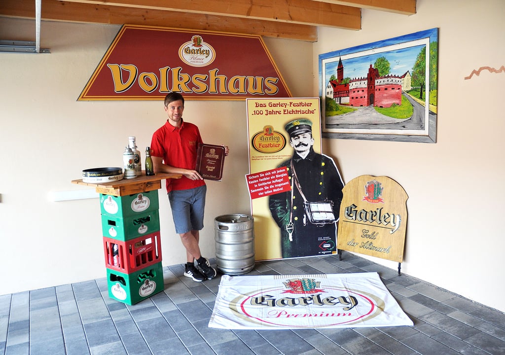 Neben Fahnen, Aufsteller, Fässer, verschiedenen Kisten und alte Bügelflaschen hat Matthias Lübke im vergangenen Jahr auch ein hölzernes Schild mit „Garley, Gold der Altmark“ erwerben können (rechts an der Wand), das zur Traditionskutsche gehört. Es wurde hinter den Kutschbock gesteckt.