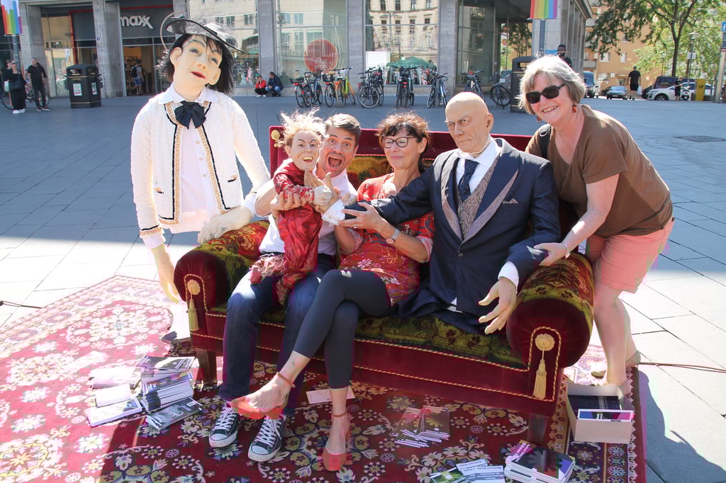 Boris Kehrmann von der Oper Halle sowie Ines Steinmetzger und Ingrid Walter vom Förderverein des Puppentheater posieren auf dem Sofa, auf dem jeder Passant Platz nehmen kann.