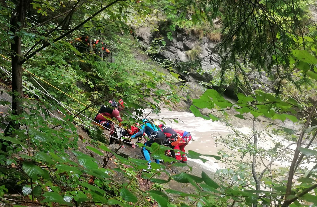 Retter arbeiten an einem Steilhang am Flussufer. Eine Frau wird vermisst, nachdem ihre Gruppe beim sogenannten Canyoning in der Starzlachklamm bei Sonthofen (Landkreises Oberallgäu) von einer Sturzflut überrascht wurde.