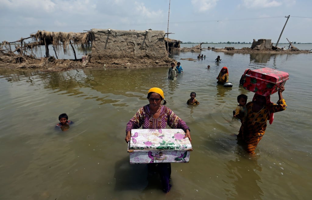 Frauen tragen Habseligkeiten aus einem durch heftige Regenfälle überschwemmten Haus im Bezirk Qambar Shahdadkot in der pakistanischen Provinz Sindh.