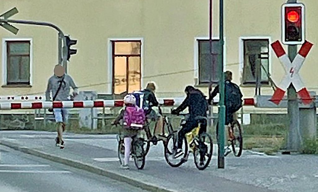 Trotz geschlossener Schranken überquert ein Erwachsener die Gleisanlagen in Tangerhütte. Kinder schauen zu.