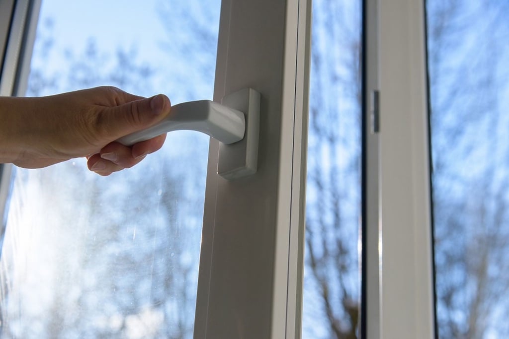 Eine Person öffnet ein Fenster in einem Wohnhaus.