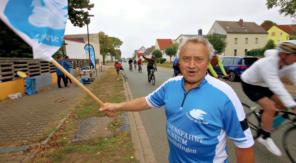 Horst Schäfer begrüßt die Radfahrer mit der Fahne des Friedensfahrtmuseums in Kleinmühlingen. Hier hat er einen Versorgungsstand aufgebaut. Supermärkte aus Schönebeck und Calbe haben ihm dafür Getränke kostenlos zur Verfügung gestellt, schildert er.