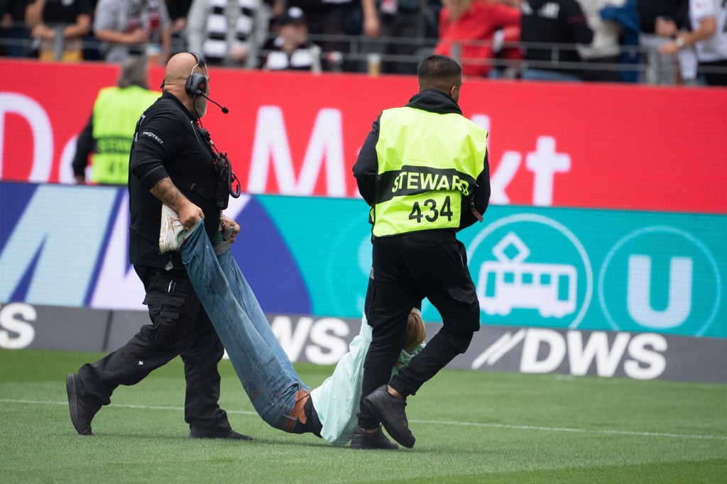 Ordner tragen Demonstrierende mit Aufdrucken gegen den Klimawandel auf ihren T-Shirts vom Feld.