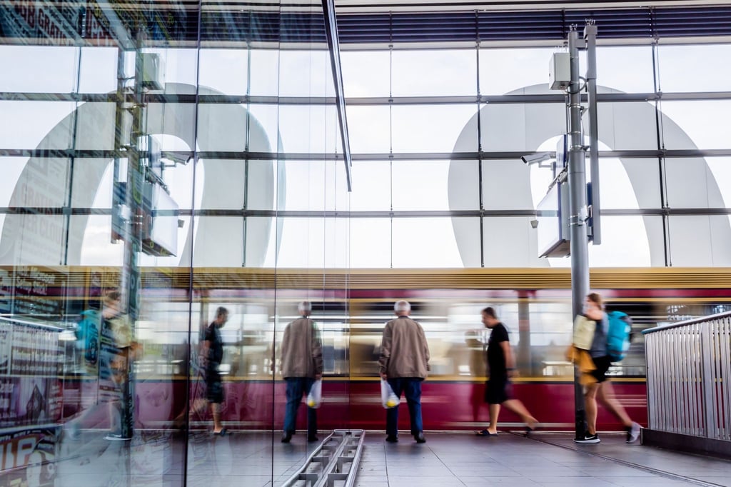 Eine S-Bahn fährt am Berliner Bahnhof Ostkreuz ein und spiegelt sich in Glasscheibe.