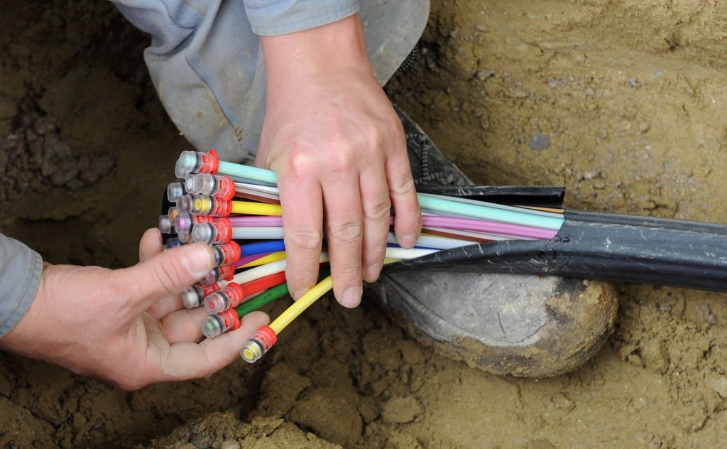 Ein Mann fächert ein Glasfaser-Kabel mit farbigen Einzelsträngen auseinander. In Schkopau werden gerade Anschlüsse gelegt.