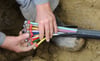 Ein Mann fächert ein Glasfaser-Kabel mit farbigen Einzelsträngen auseinander. In Schkopau werden gerade Anschlüsse gelegt. 