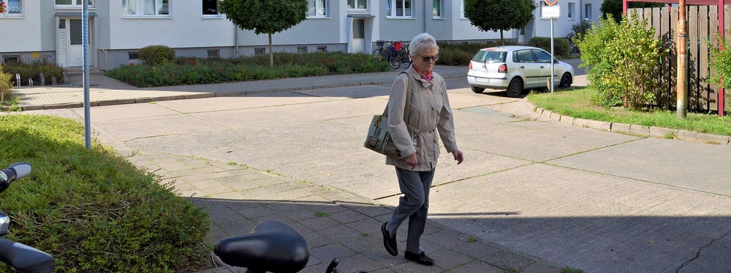 Rosa Rösler (83) auf dem Weg zum Büro der Wobau, wo sie die Einwilligung in die Erhöhung der monatlichen Heizkostenvorauszahlung abgeben will. Im Hintergrund ist einer der Wohnblöcke zu sehen, die betroffen sind.