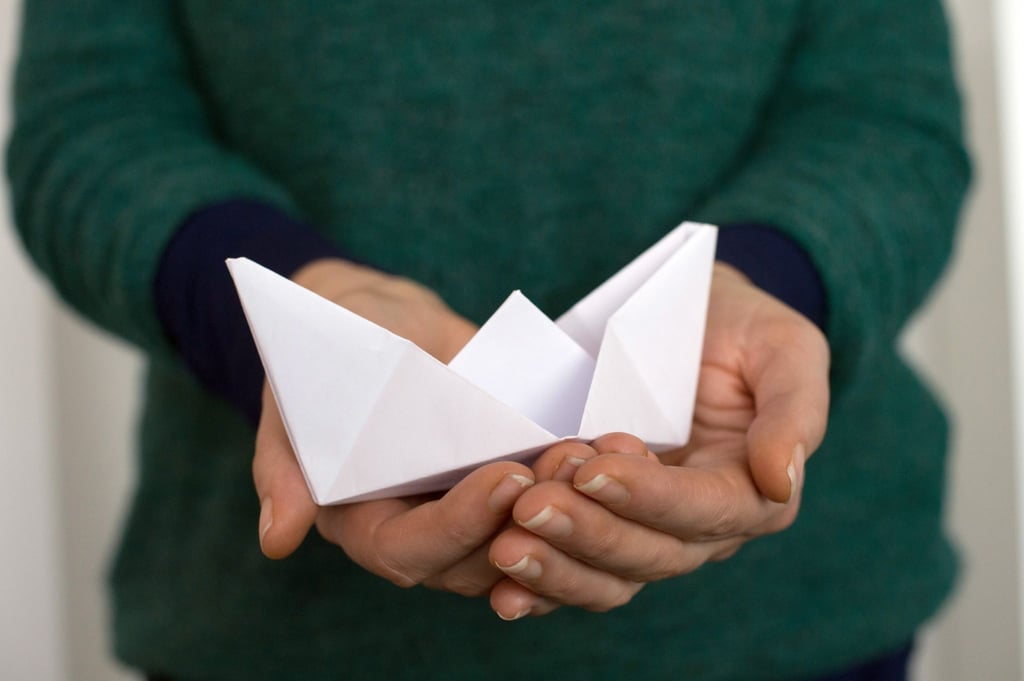 Eine Mitarbeiterin des Psychosozialen Zentrums hält ein Papierschiff in den Händen.