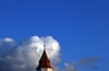 Wolken türmen sich hinter einem Kirchturm.