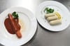 Eine vegane Currywurst und vegane Weißwürste liegen auf Tellern an der Essensausgabe im Hofbräuzelt auf dem Oktoberfest.